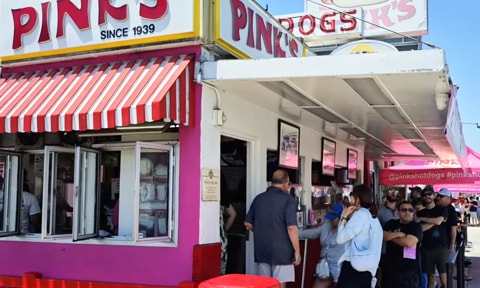 Front of Pink's Hot Dogs with a line of people waiting in line talking about their favorite hot dogs.